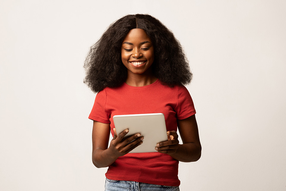 a young black woman smiles while holding and reading a tablet computer